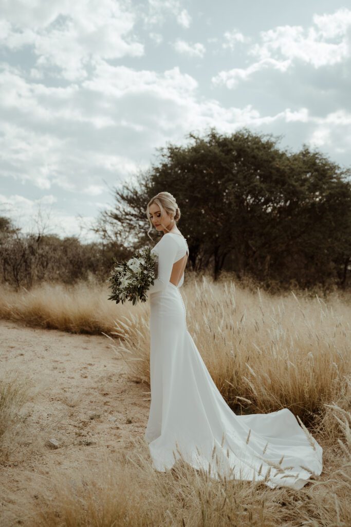 A beautiful bride standing in a field, wearing a long sleeve, plain, elegant wedding dress.