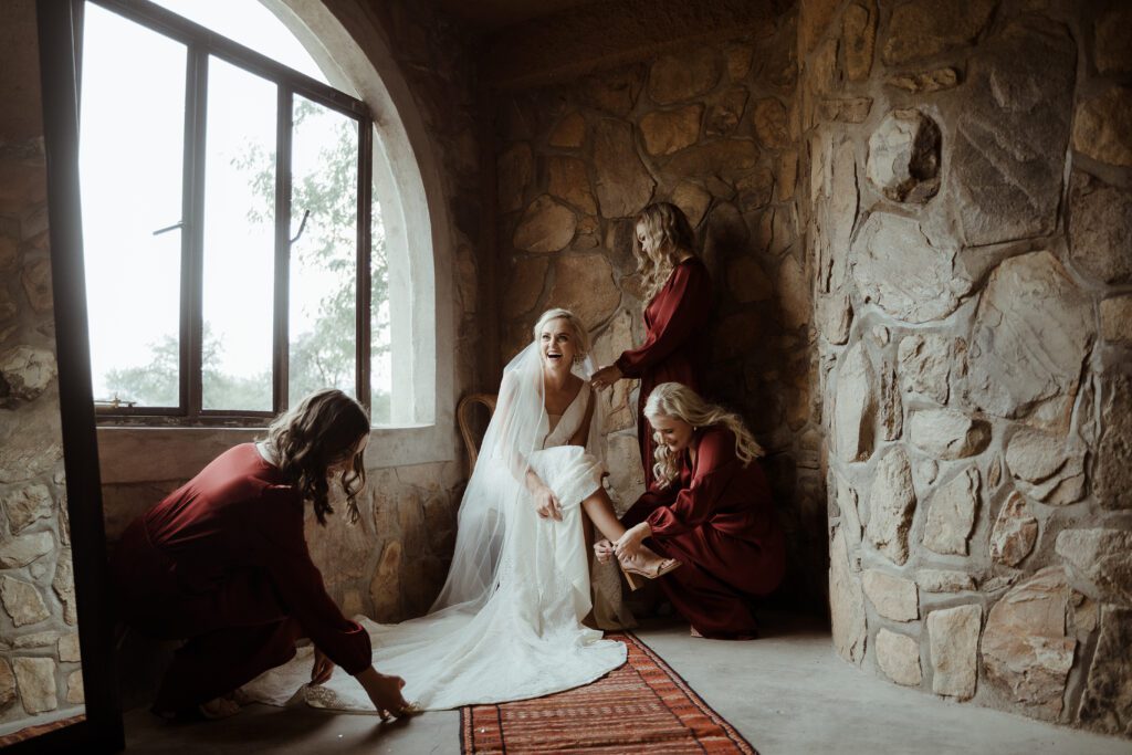 A beautiful bride being helped to get dressed by her bridesmaids, wearing a beautiful bohemian style gown.