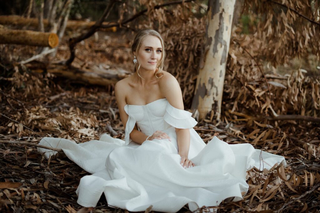 A beautiful bride sitting in a field, wearing a wedding dress.