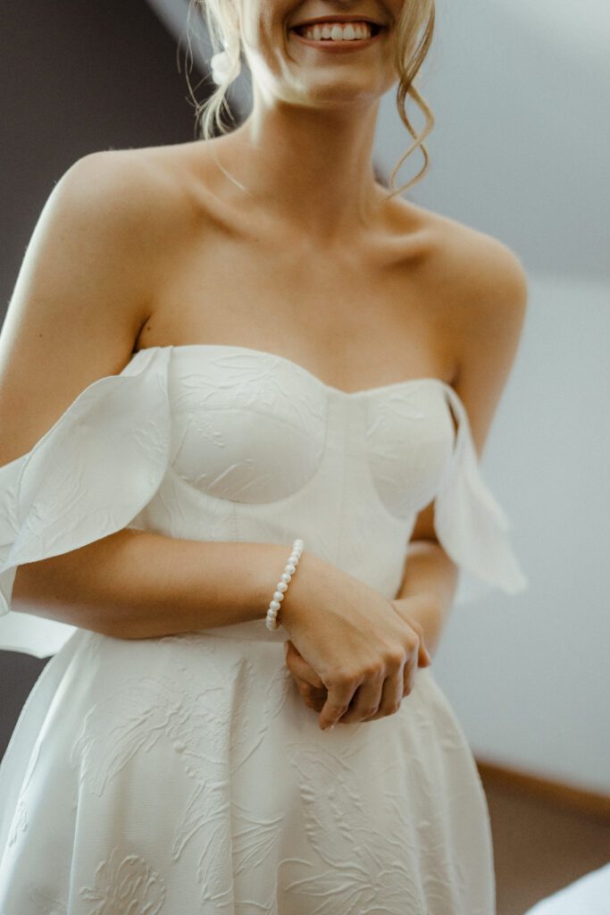 Torso of a bride displaying detail on her off-shoulder wedding dress.